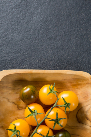 Overhead view of cherry tomatoes in wooden plate on gray slateの写真素材