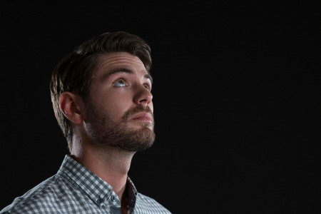 Thoughtful man standing against black backgroundの写真素材