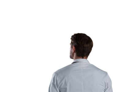 Rear view of thoughtful male doctor standing against white backgroundの写真素材