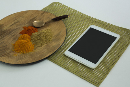 Close-up of various type of spices on wooden board with digital tablet