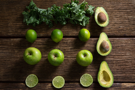 Overhead of mustard greens, lemon, avocado and green apple arranged on wooden tableの写真素材