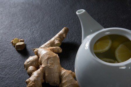 Close-up of lemon slice in teapot with ginger on black background