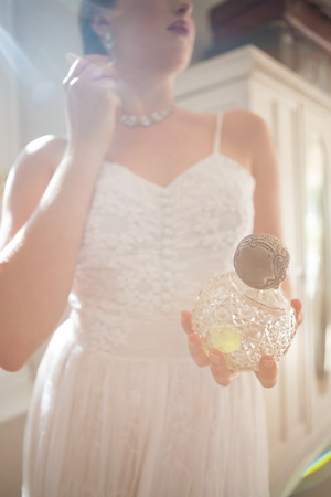 Low angle view of beautiful bride holding perfume while wearing earring at homeの写真素材