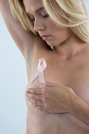 Woman covering breast while looking at pink ribbon against gray backgroundの写真素材
