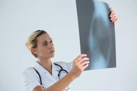 Female doctor examining X-ray while standing against gray backgroundの写真素材