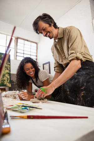 Man assisting woman in molding clay during drawing classの写真素材