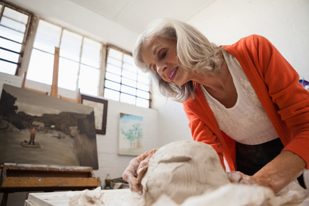 Attentive senior woman shaping a molded clay in drawing classの写真素材