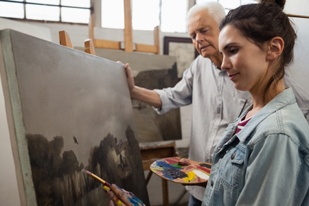 Senior man watching while artist painting on canvas in drawing classの写真素材