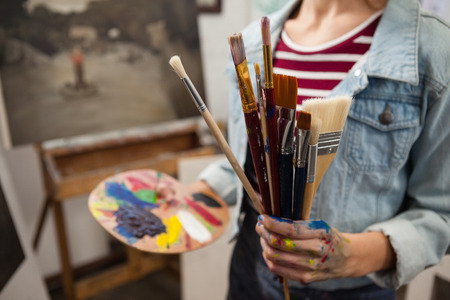 Mid-section of woman holding various brushes in drawing classの写真素材