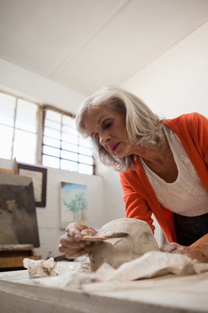 Attentive senior woman shaping a molded clay in drawing classの写真素材