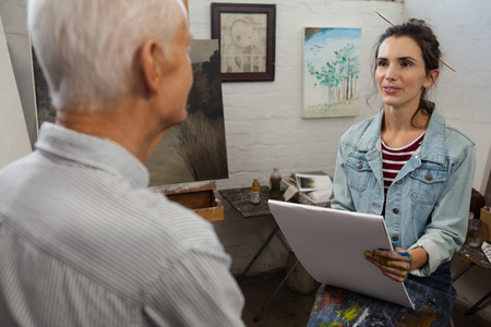Woman interacting with senior man while sketching on canvas in drawing classの写真素材
