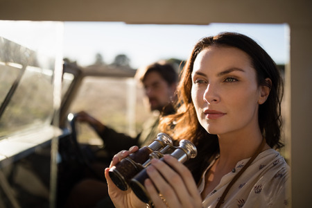 Thoughtful woman sitting with binoculars in vehicle during safari vacationの写真素材
