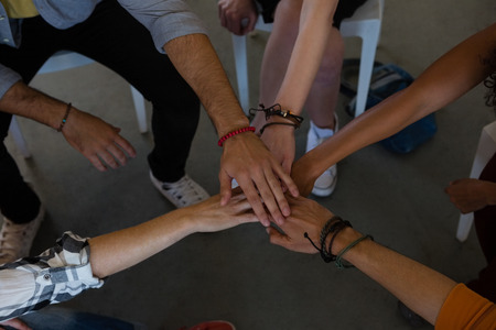 High angle view of adult students stacking hands while sitting on chair in art studioの写真素材
