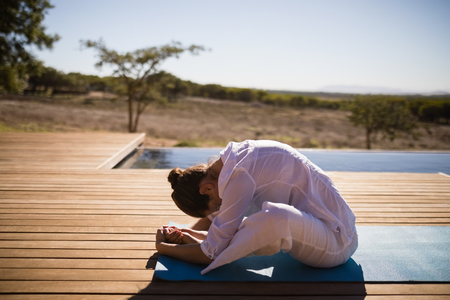 Woman practicing yoga on at poolside on a sunny dayの写真素材