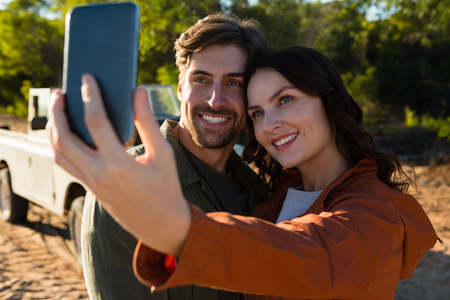 Smiling young woman with man taking selfie on fieldの写真素材