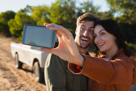 Happy young woman taking selfie with man on fieldの写真素材