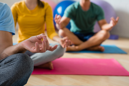 Midsection of yoga instructor with students meditating in lotus position at health clubの写真素材