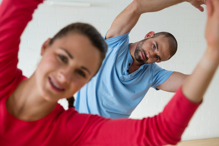 Portrait of male instructor exercising with female student in health clubの写真素材