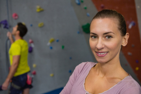 Portrait of confident athlete standing against man rock climbing in health clubの写真素材