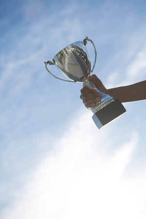 Close-up of hand holding a trophy against sky and cloudの写真素材