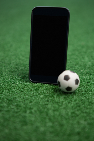 Close-up of football and mobile phone on artificial grassの写真素材