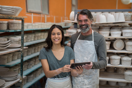 Portrait of male and female potter holding digital tablet in pottery workshop