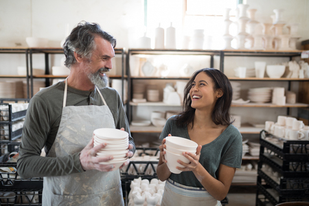 Male and female potter holding ceramic bowls in pottery workshopの写真素材
