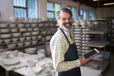 Portrait of male potter using digital tablet in pottery workshopの写真素材