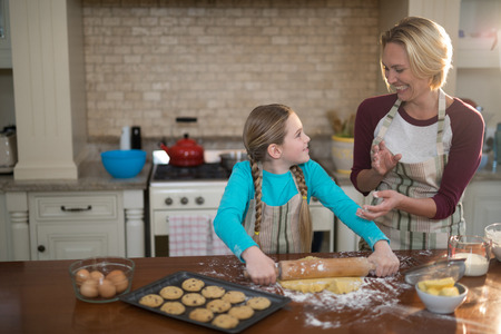 Happy mother and daughter having fun while preparing cookies in kitchen at homeの写真素材