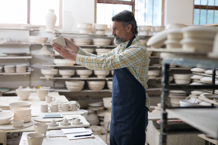 Male potter checking craft product in workshopの写真素材
