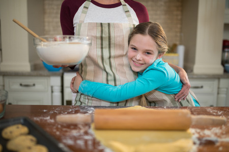 Happy daughter hugging mother while preparing cookies in kitchenの写真素材