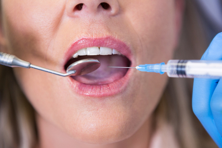 High angle view of dentist holding syringe by patient mouth at medical clinicの写真素材