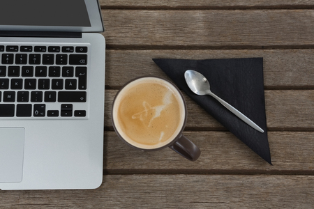 Overhead of laptop, spoon, napkin and coffee on wooden plankの写真素材