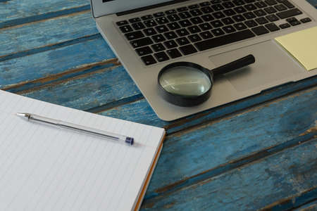 Close-up of blank book, magnifying glass and laptop on wooden plankの写真素材