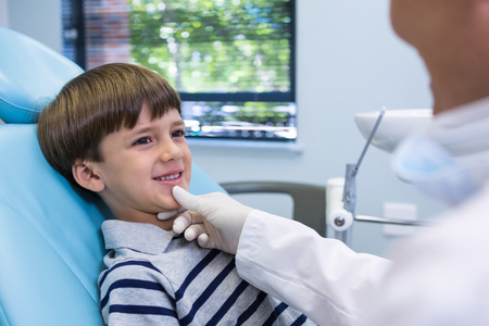 Smiling boy looking at dentist while sitting on chair in medical clinicの写真素材