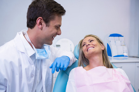 Smiling patient looking at dentist while sitting on chair at dental clinicの写真素材