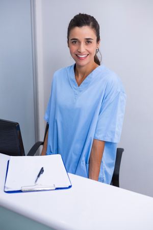 Portrait of smiling doctor standing at desk against wall in dental clinicの写真素材