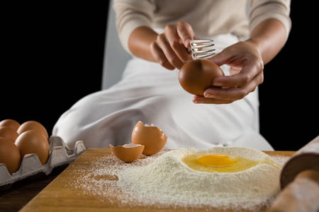 Mid-section of man breaking eggs in the flour on wooden boardの写真素材