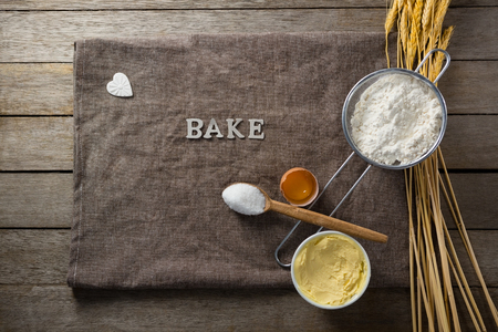 Over head view of wheat stem, wear flour, sieve, spoon placed over a cloth on wooden tableの写真素材