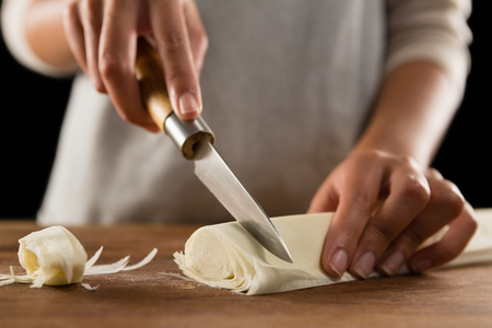 Close-up of woman slicing dough on chopping boardの写真素材