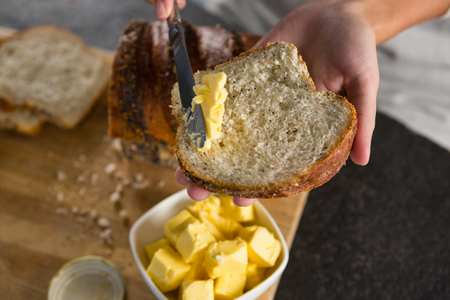 Close-up of woman applying butter over multigrain bread sliceの写真素材