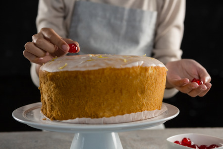Mid section of woman toping a fresh baked cake with cherry