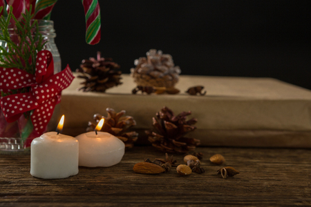 Close up illuminated candles with pine cones and gift box on table against black backgroundの写真素材