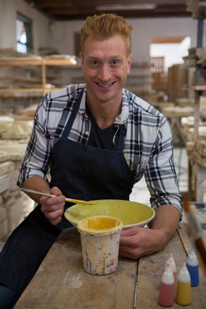 Portrait of male potter painting a bowl in pottery workshopの写真素材