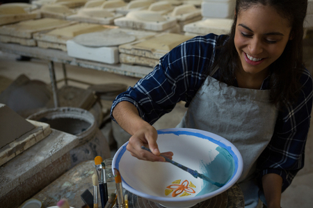 Female potter painting a bowl in pottery workshopの写真素材