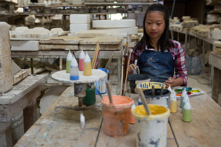 Portrait of girl painting bowl in pottery workshopの写真素材