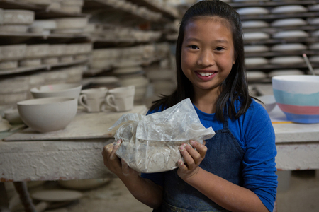 Portrait of happy girl holding clay in pottery workshopの写真素材
