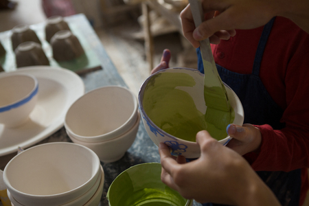 Mid section of female potter and boy painting bowl in pottery workshopの写真素材