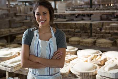 Confident female potter standing with arms crossed in pottery workshopの写真素材