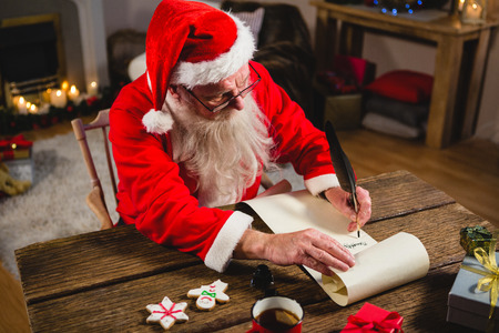 Santa Claus writing on scroll in living room at homeの写真素材